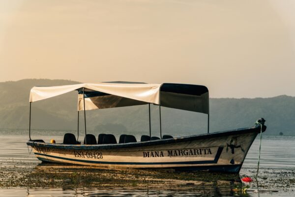 A serene view of a boat on Lake Coatepeque in El Salvador, captured at sunrise.