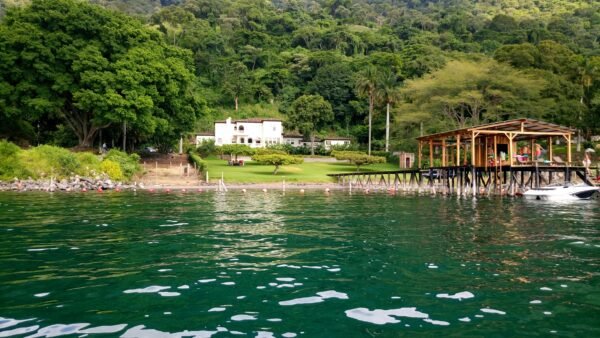 A beautiful lakefront house surrounded by lush greenery and a wooden dock at Coatepeque Lake.